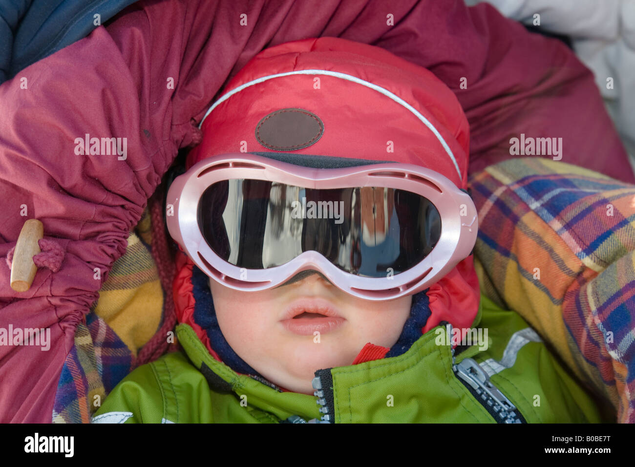 A one year old girl wearing ski glasses lies in a buggy, well protected against the cold Stock Photo
