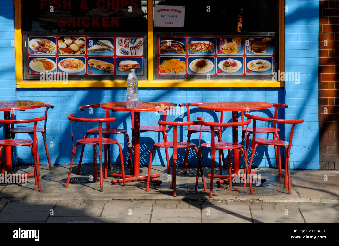 Red metal tables and chairs on pavement before blue and yellow cafe, Marchmont Street, Bloomsbury, London, England Stock Photo