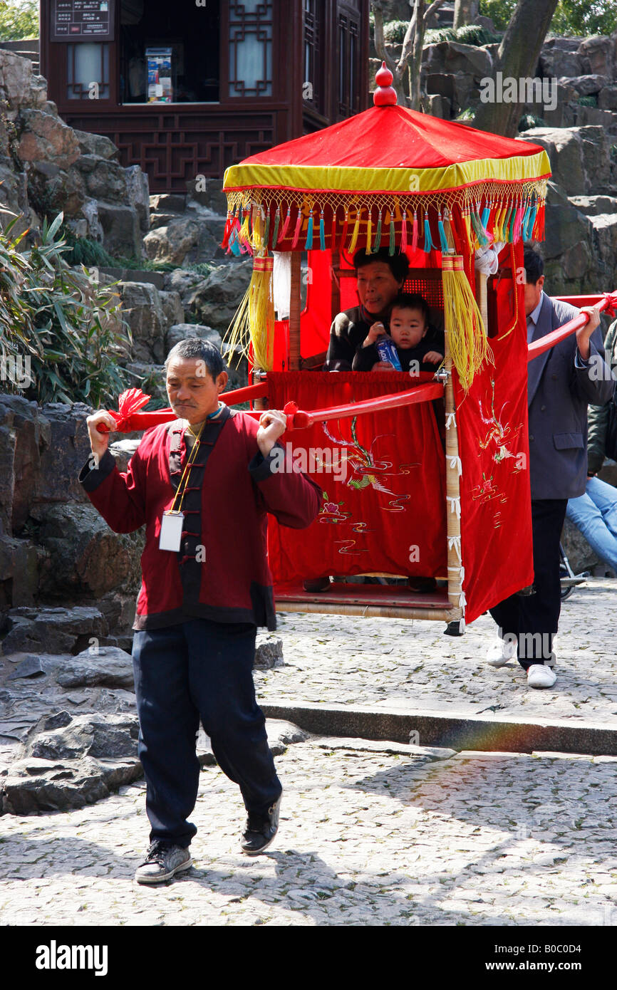 Grandmother and child being carried in a Sedan Chair to the top of Tiger Hill to see the leaning Pagoda. Stock Photo