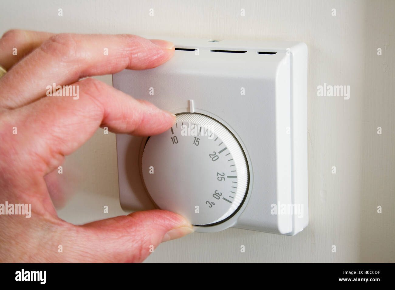Pensioner's hand turning down home central heating thermostat set at low temperature to reduce household energy costs and carbon footprint. England UK Stock Photo