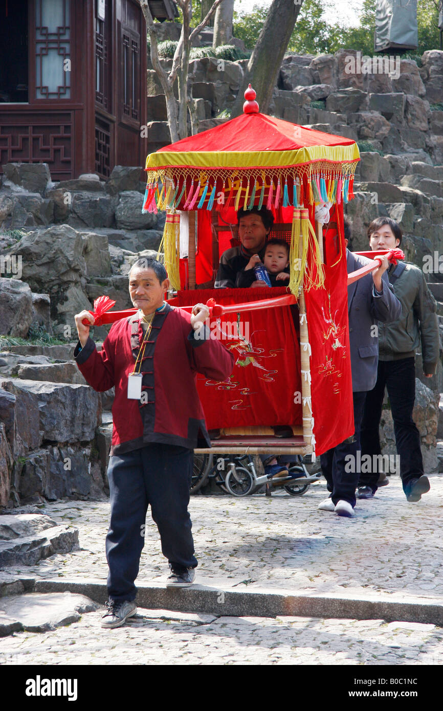 Grandmother and child being carried in a Sedan Chair to the top of Tiger Hill to see the leaning Pagoda. Stock Photo