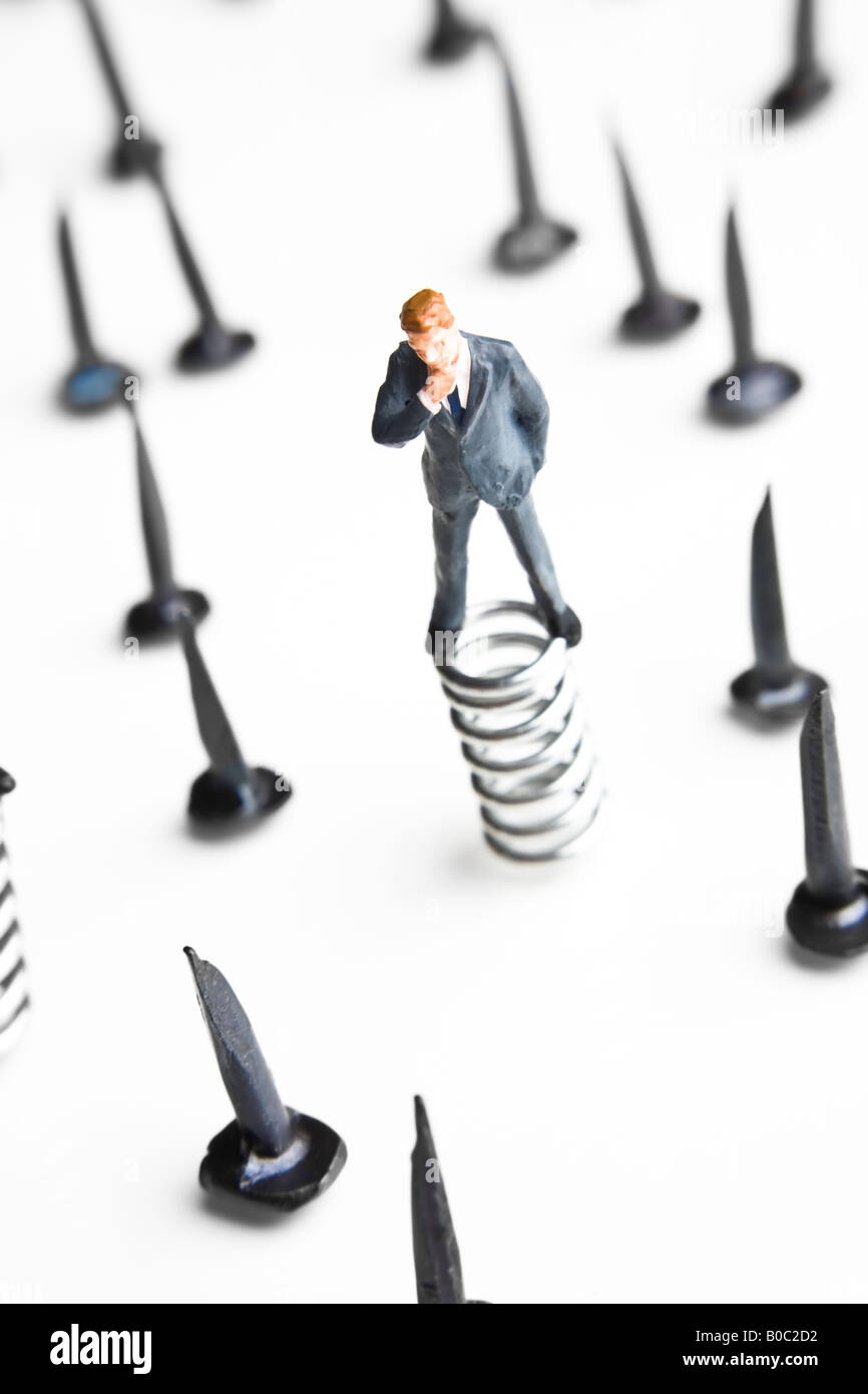 Businessman figurine standing on springs surrounded by tacks Stock Photo