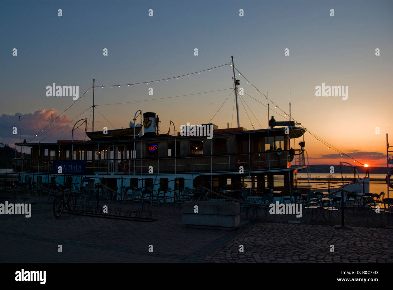A boat at a pier at dusk with sun setting in the background Stock Photo