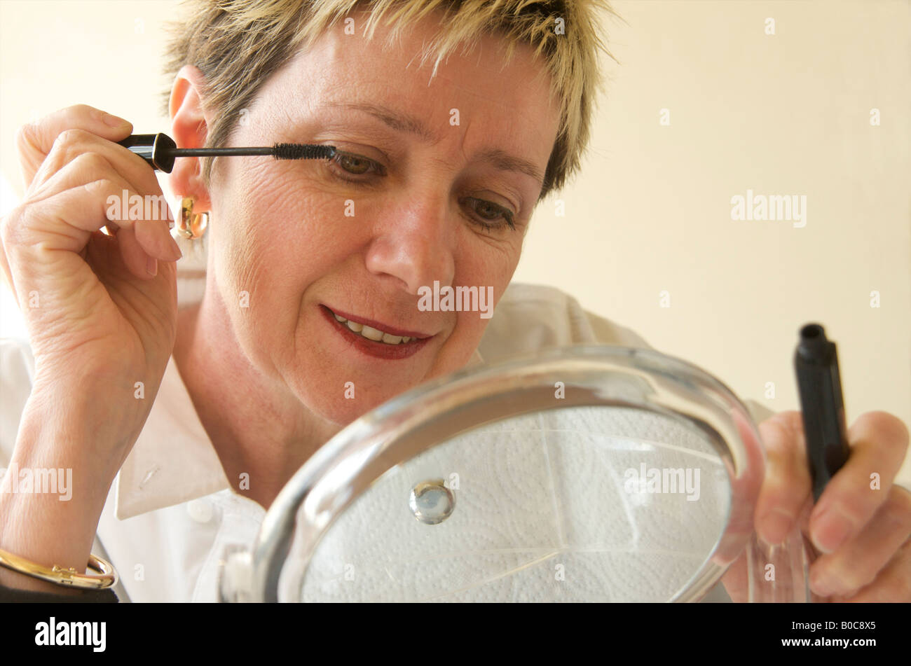 Mature woman putting on make up / mascara Stock Photo