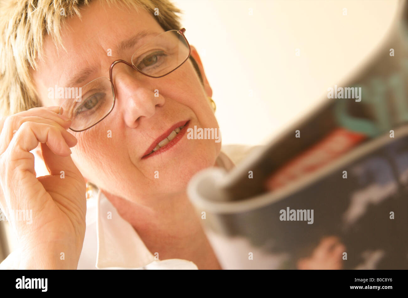 Mature, late middle aged woman trying to read a magazine with poor eyesight Stock Photo