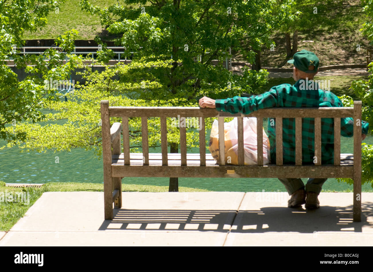 A Senior Man Rests On A Park Bench Overlooking A Small Lake On A