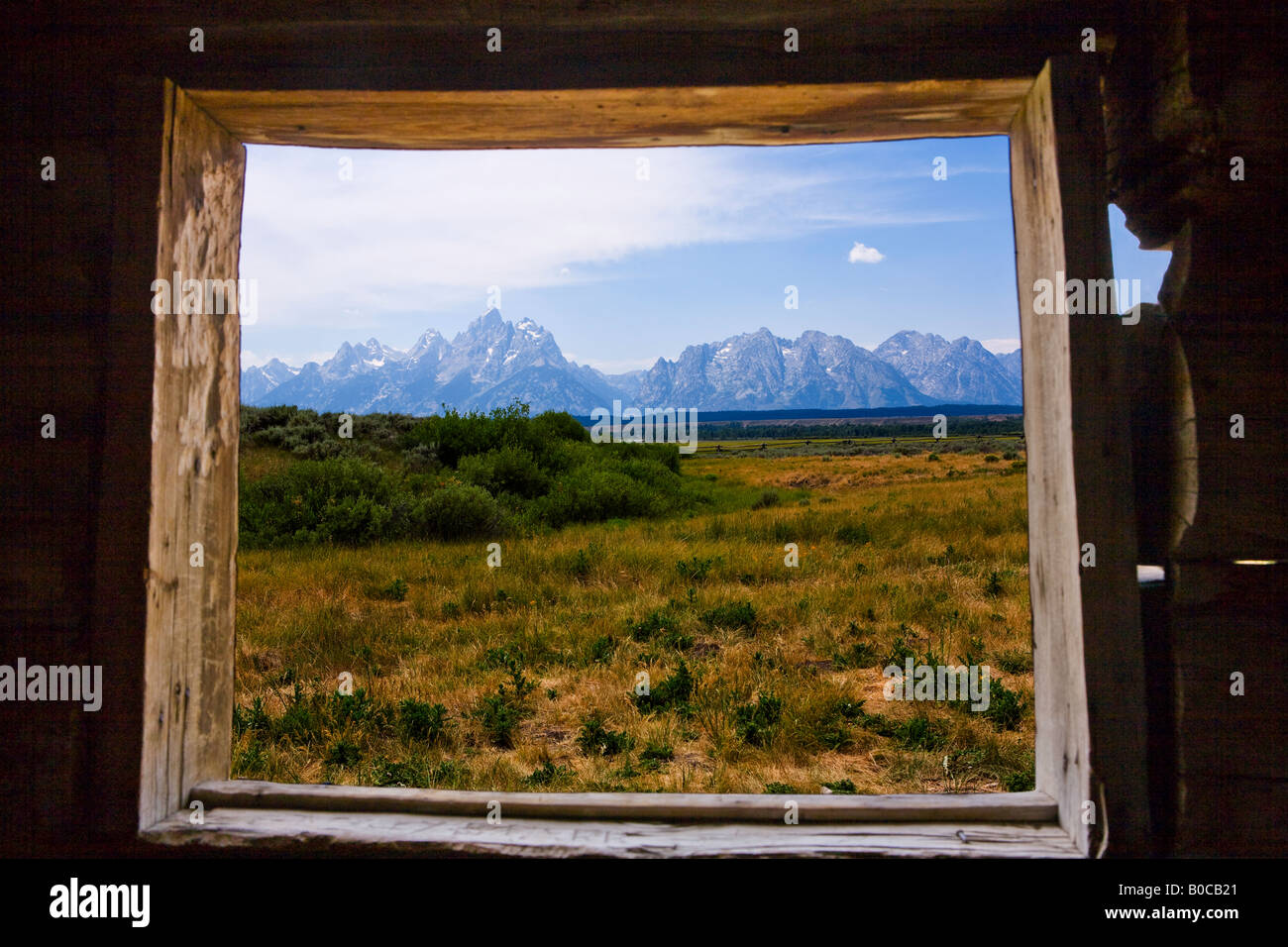 Image of the Grand Teton Mountains looking through a window of a log cabin Stock Photo