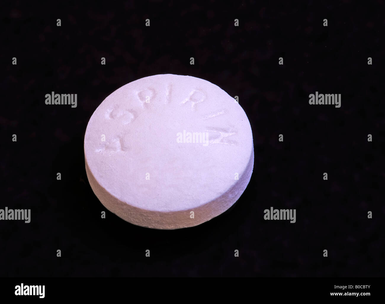 Image of a single asprin tablet laying face up on a black background ...