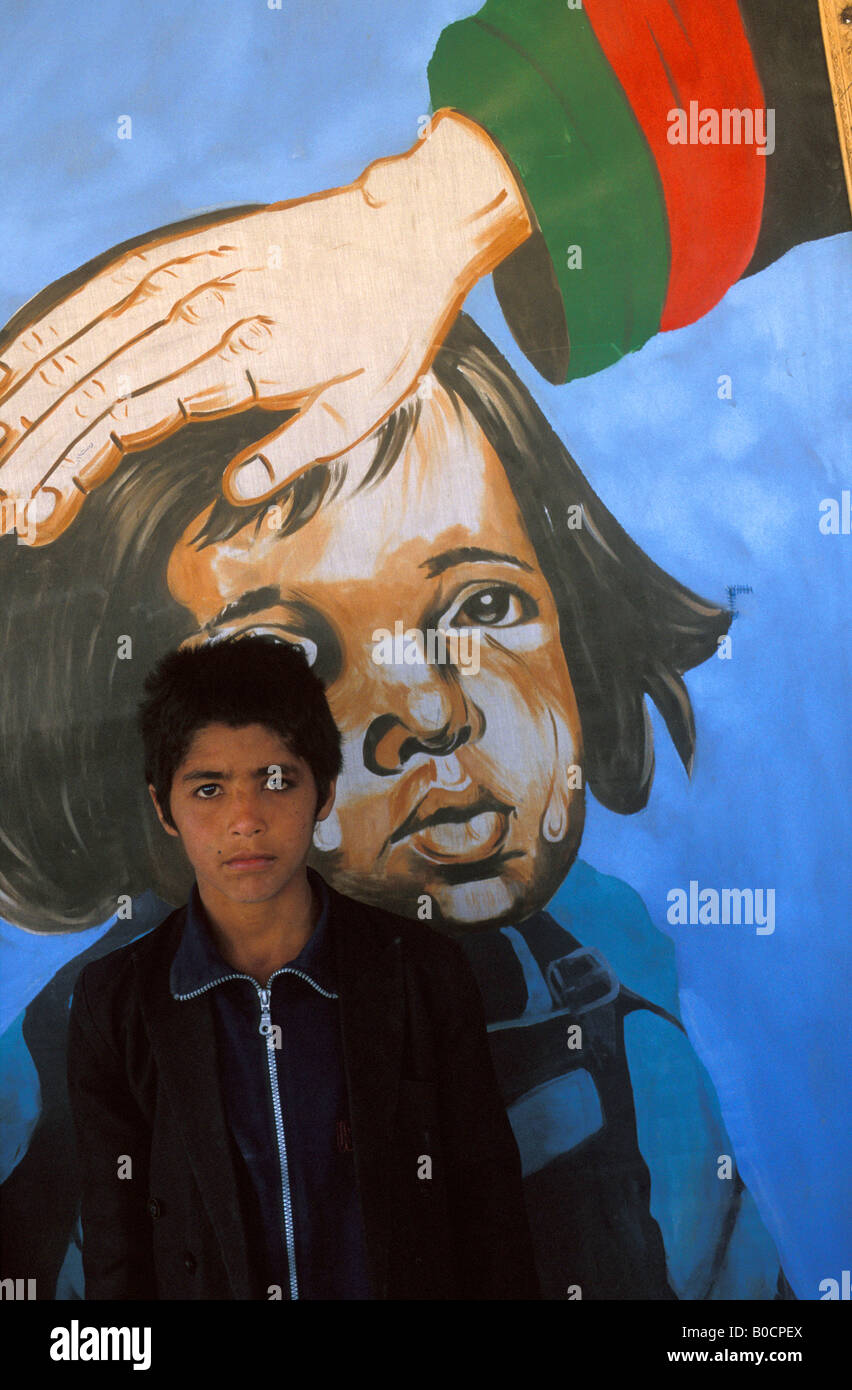 Kabul portrait of a boy in front of a painting which claims the government is taking care of the Afghan children Stock Photo