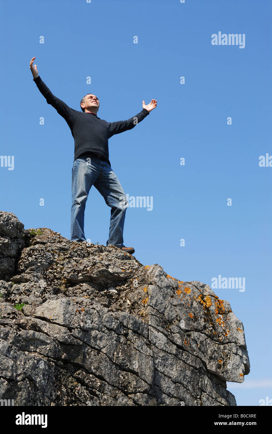 A man standing on a cliff with his arms raised to the blue sky Stock ...