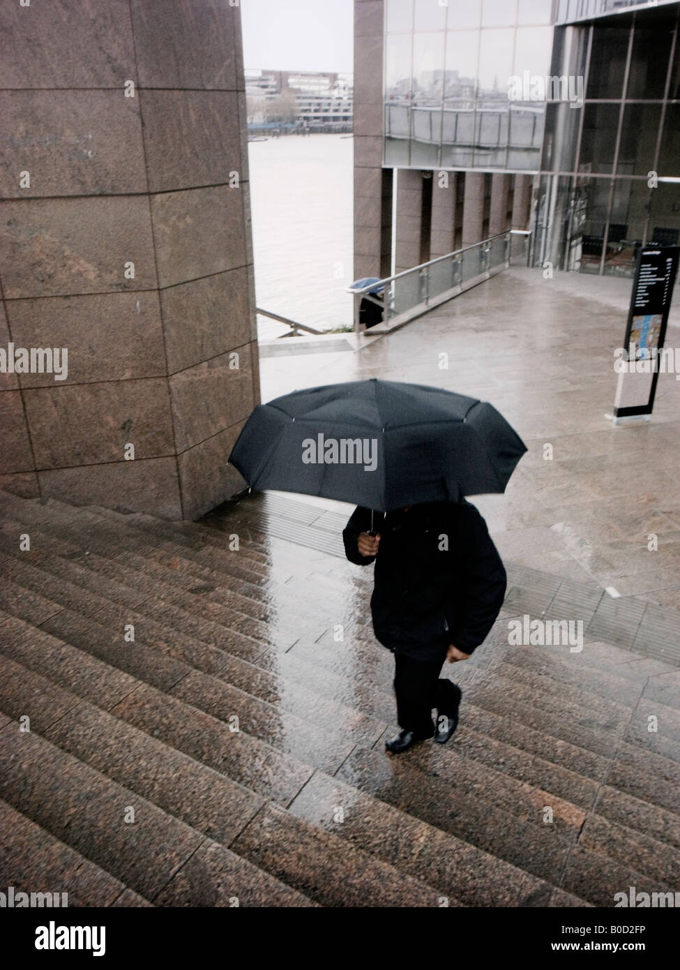 Man with umbrella runs up the steps of Number One London Bridge Building on a rainy day City Of London England Stock Photo