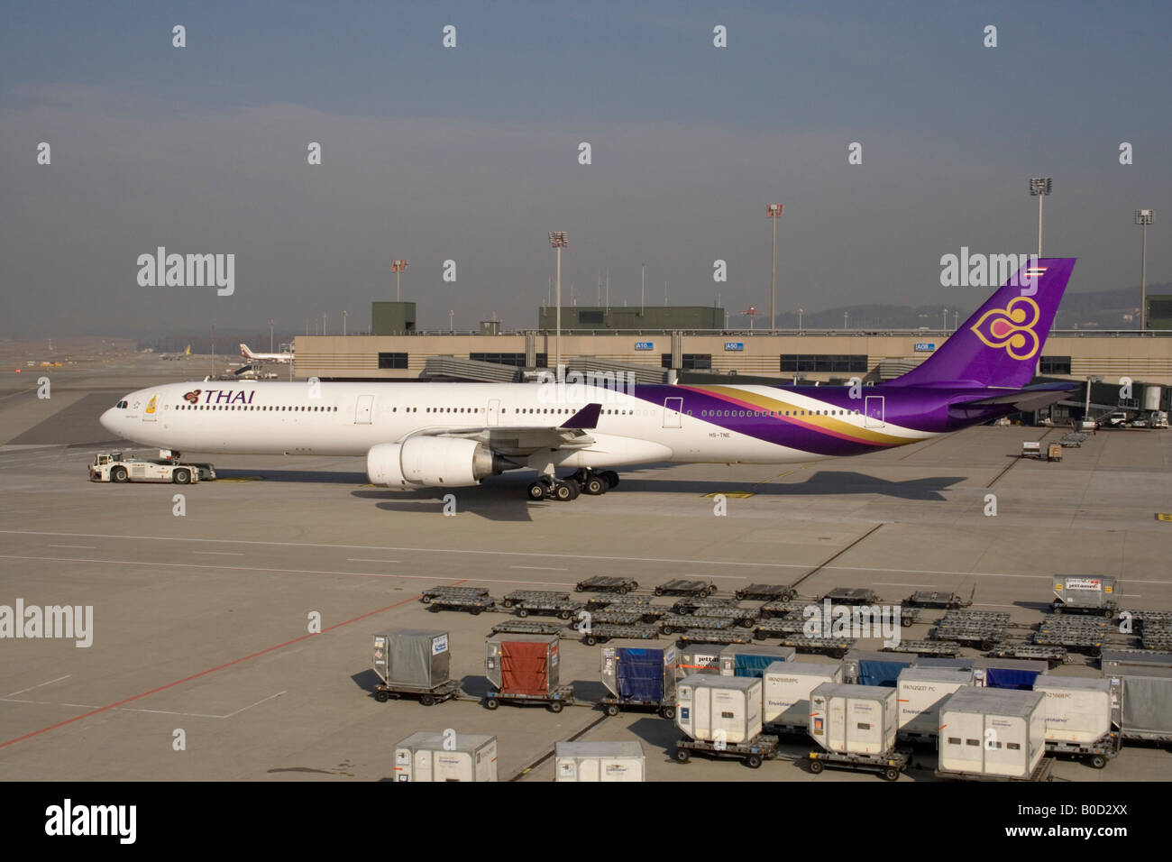 Thai Airways International Airbus A340-600 being towed to its gate at Zurich Airport, with air cargo containers in the foreground Stock Photo