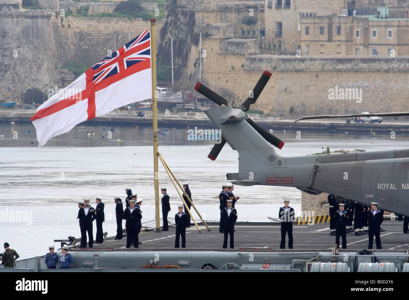 The Royal Navy aircraft carrier HMS Illustrious on arrival in Malta's Grand Harbour with sailors standing to attention beneath the White Ensign Stock Photo