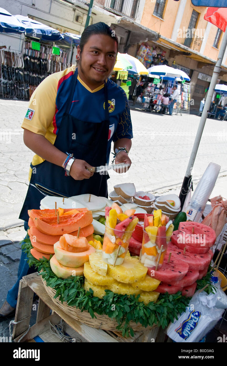 Mexican man selling sliced papayas, melons, coconuts and pineapples, for sale on street corner in Puebla, Mexico. Stock Photo