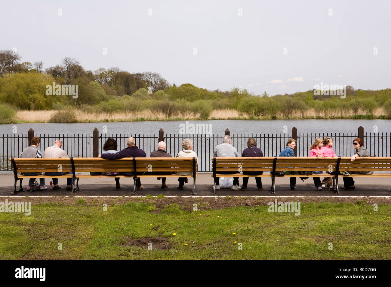 UK Cheshire Knutsford town centre people sat on benches overlooking Moor Pool Stock Photo