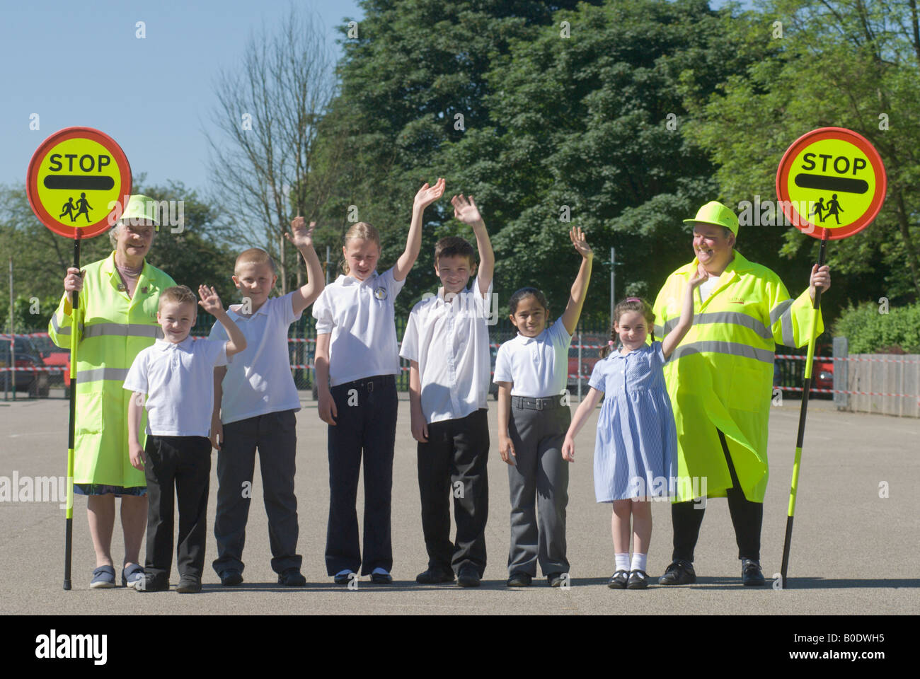 Two lollipop ladies with children waving from the school they help out at. Stock Photo