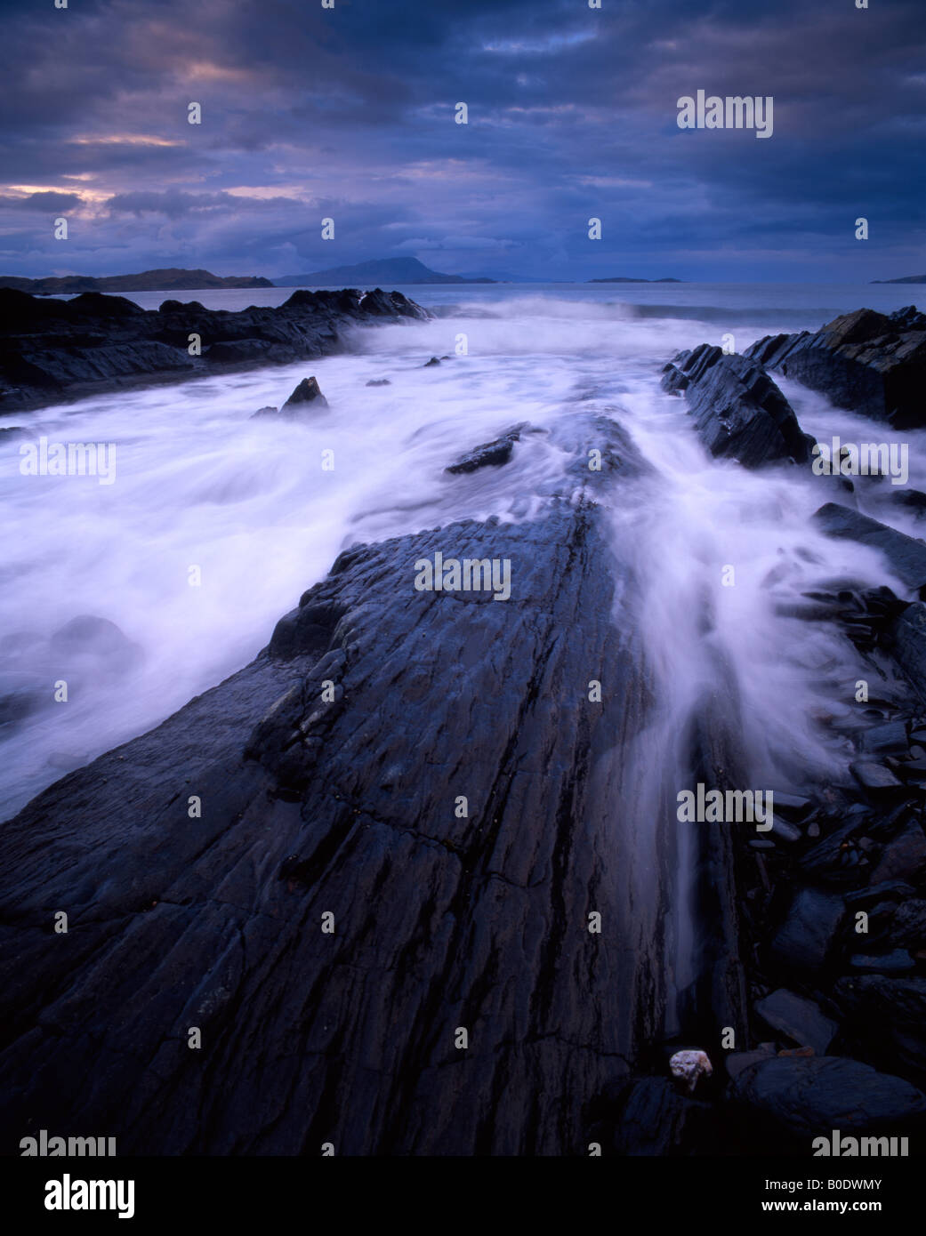 Incoming tide and dark skies on Seil with Scarba and Jura beyond, Argyll, Scotland, UK. Stock Photo