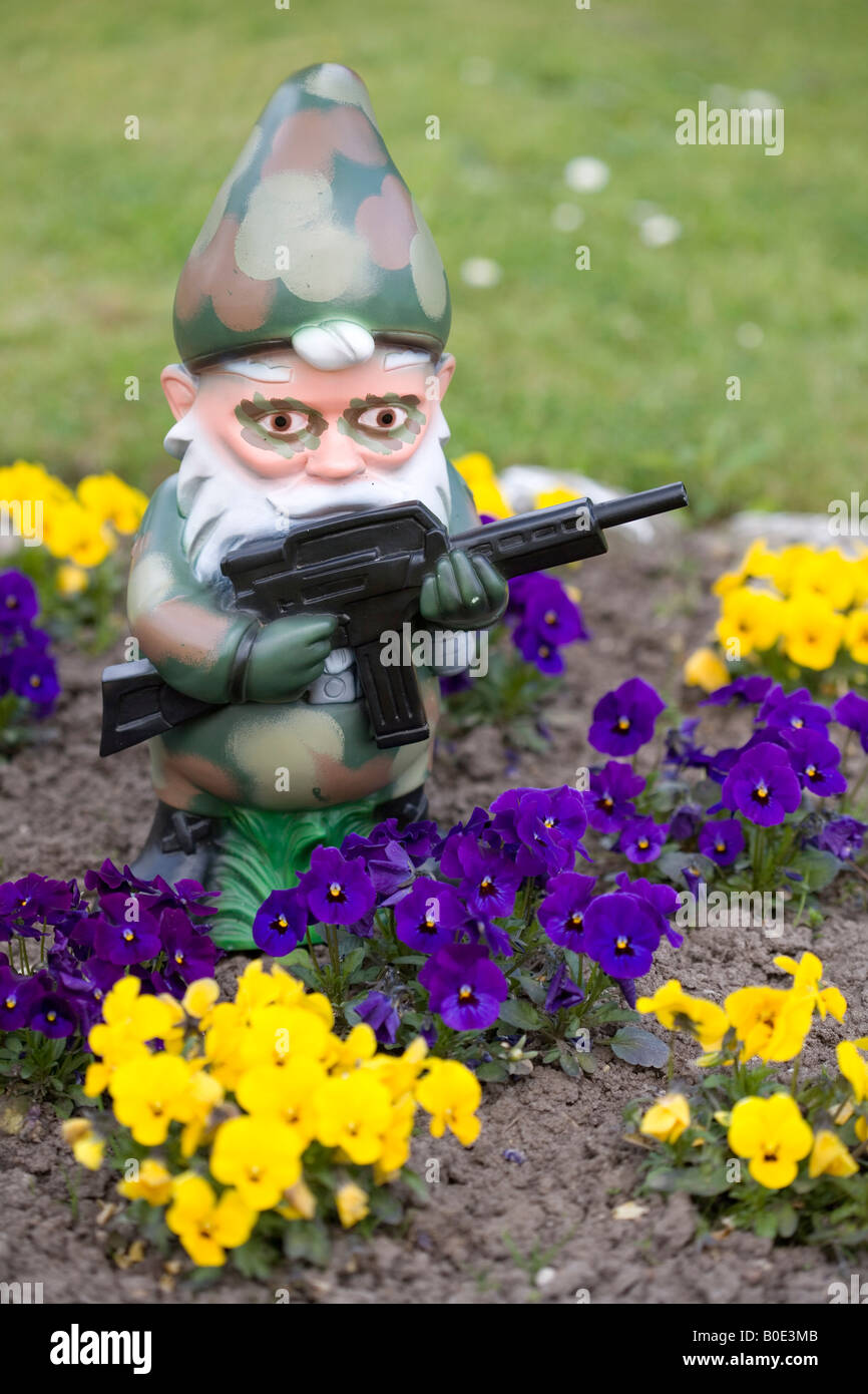 Garden Gnome In Camouflage With Machine Gun Behind Flowers Stock