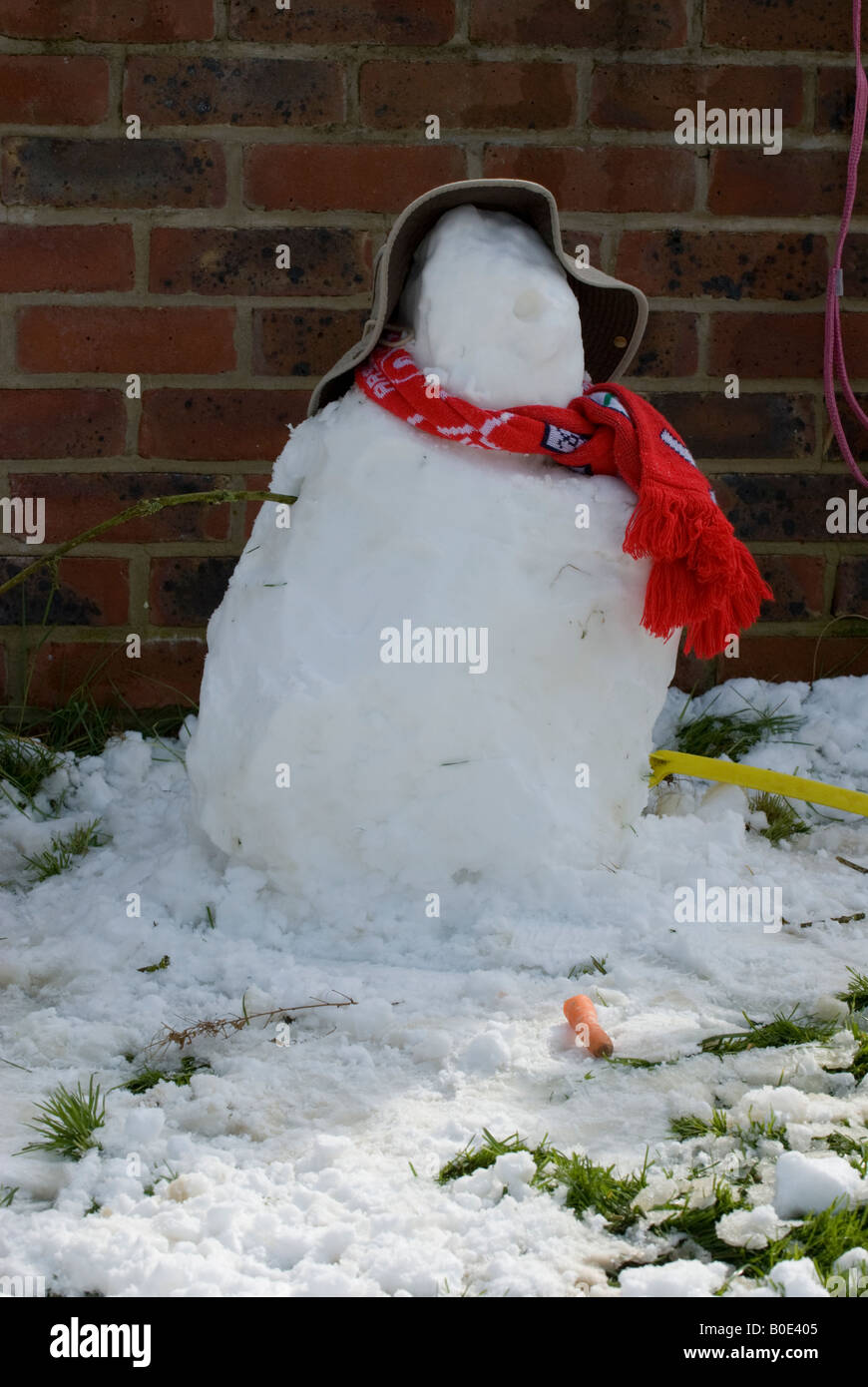 Snowman with nose on ground wearing a hat and red scarf in garden Stock Photo