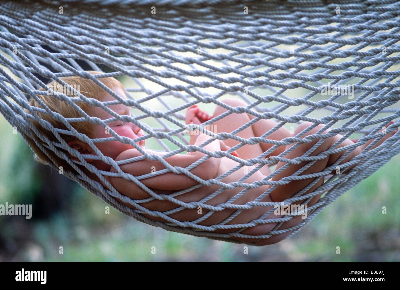An unclothed baby girl peacefully sleeps in a hammock outdoors. Stock Photo