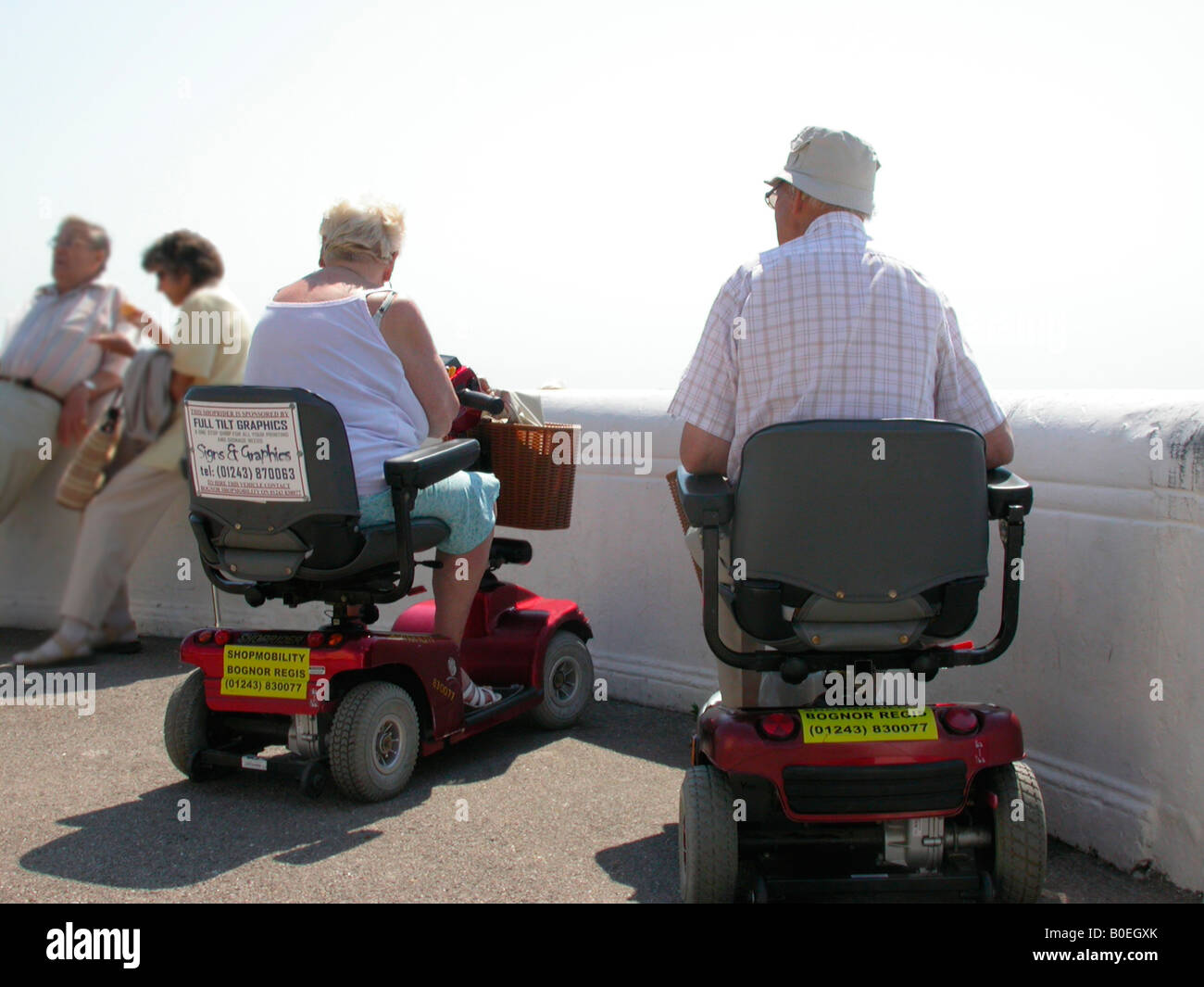 elderly couple at the seaside getting about on electronic motorised scooters on loan from Shopmobility Bognor Regis West Sussex Stock Photo