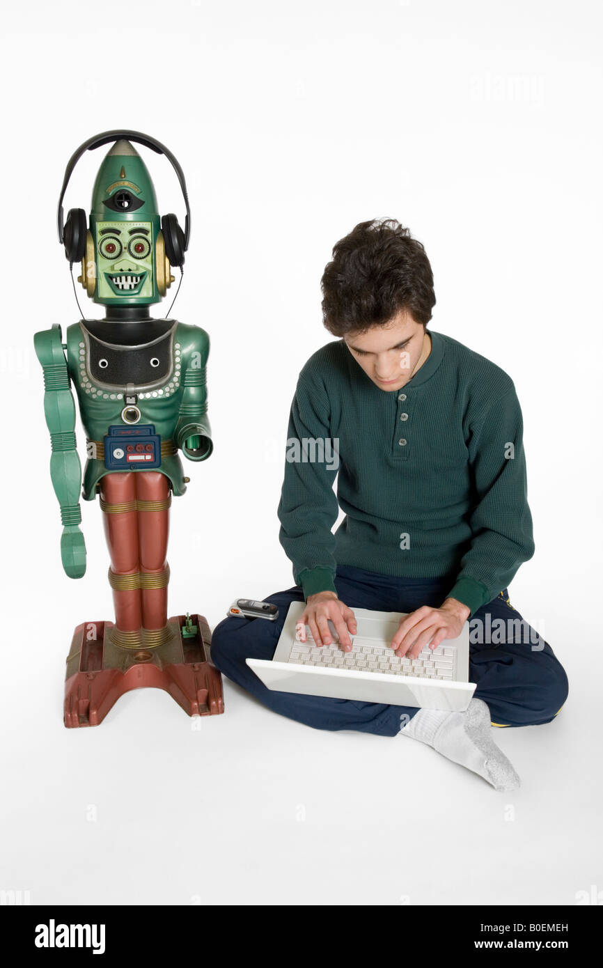 A young male teenager on a computer playing with a toy robot Stock Photo