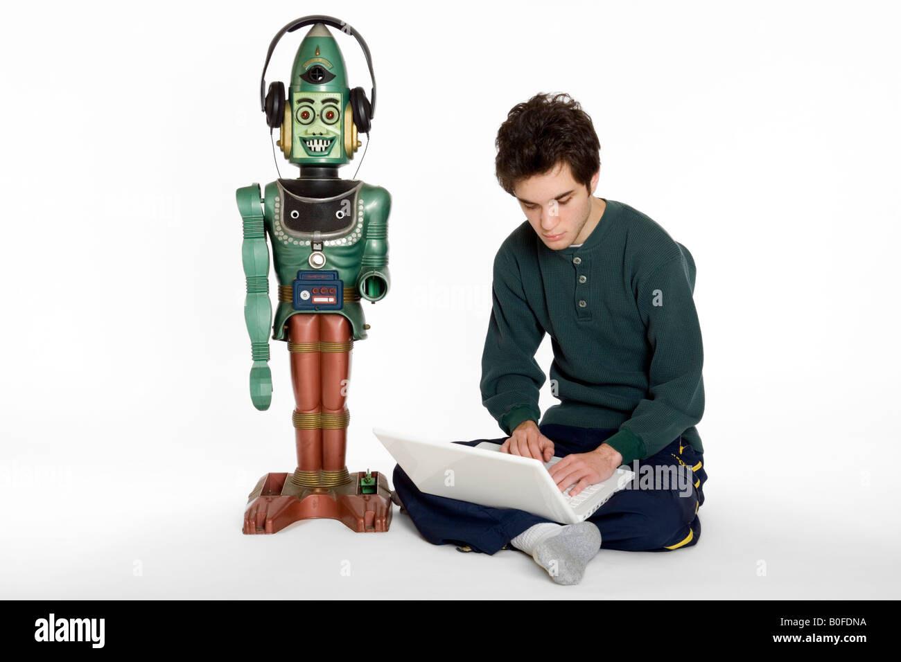 A young male teenager on a computer playing with a toy robot Stock Photo