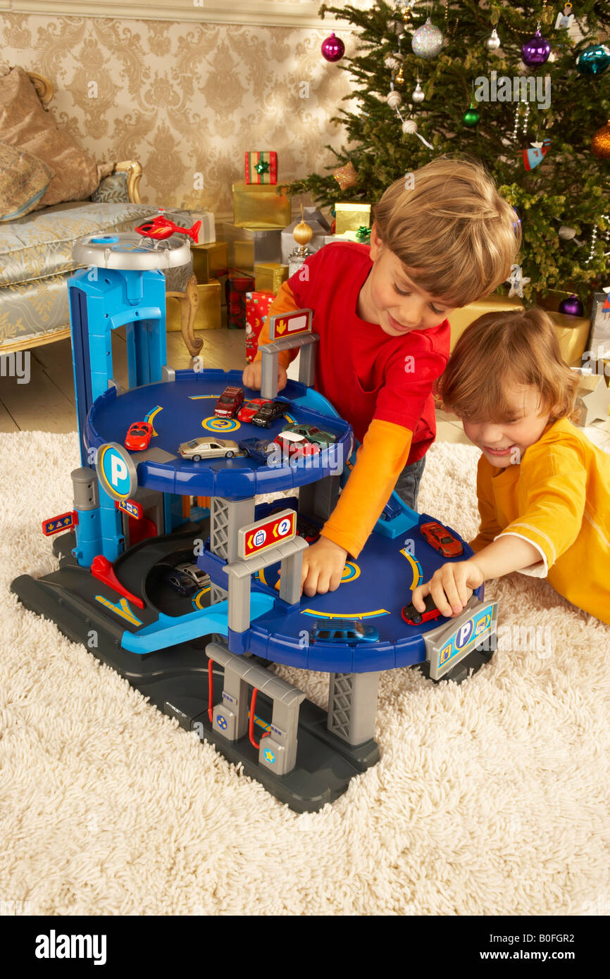 two boys play at Christmas time under the tree with a toy car garage Stock Photo