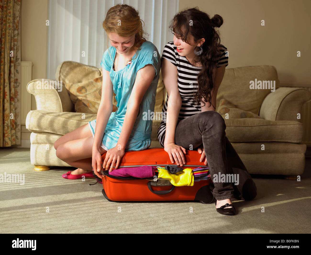 Two females trying to close suitcase Stock Photo Alamy