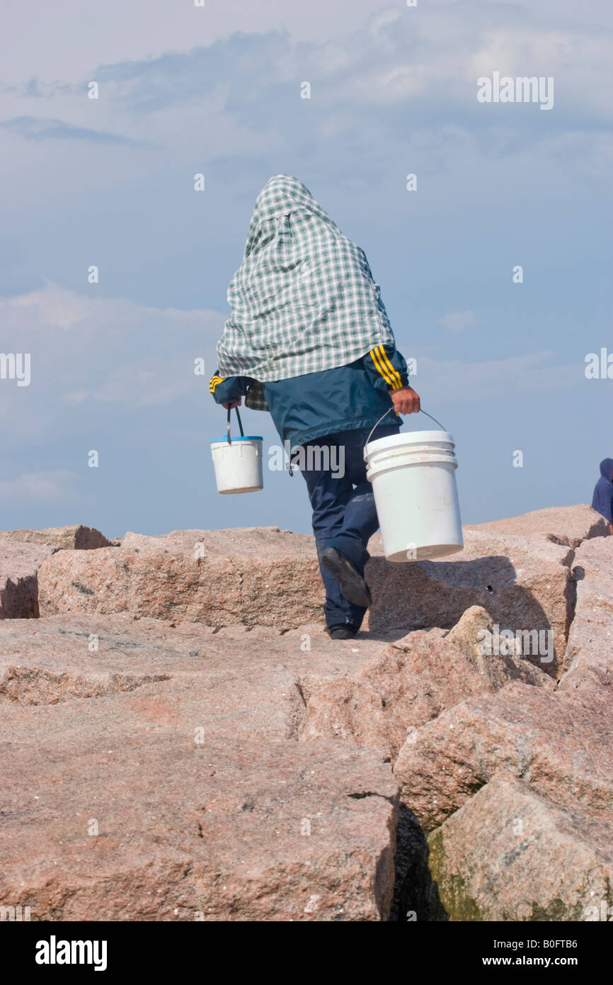 Man his head covered walking on the rocks at the beach carrying a ...