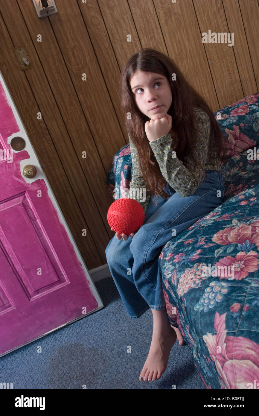 Preteen Girl Holding A Rubber Ball Sitting On A Bed In A Motel Roo