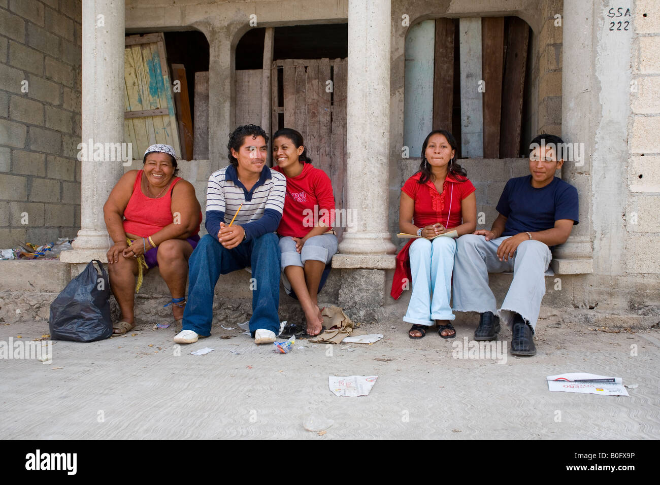 MEXICAN PEOPLE WITH MAYAN FACE CHARACTERISTICS SITING DOWN AT THE STEPS OF A BUILDING WHILE WAITING FOR THE BUS Stock Photo