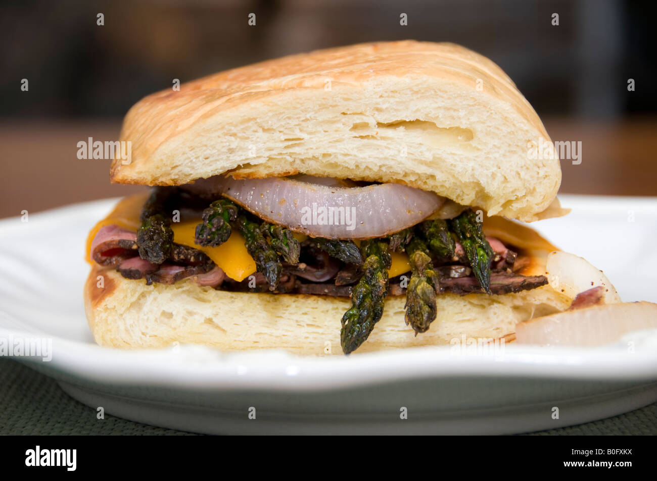 A hot sandwich made with pastrami, grilled asparagus, red onion, and