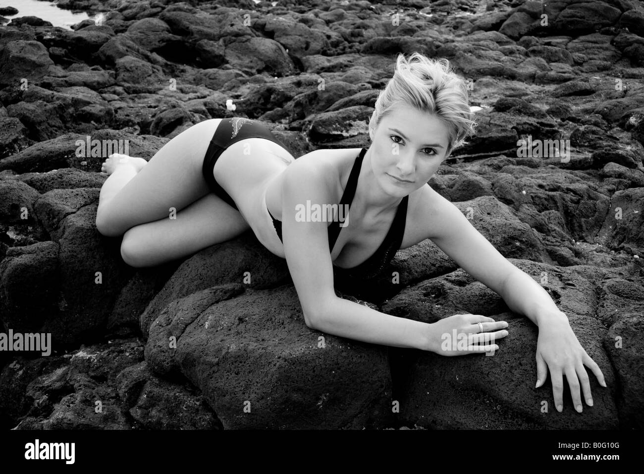 Young woman laying on lava rock beach Stock Photo