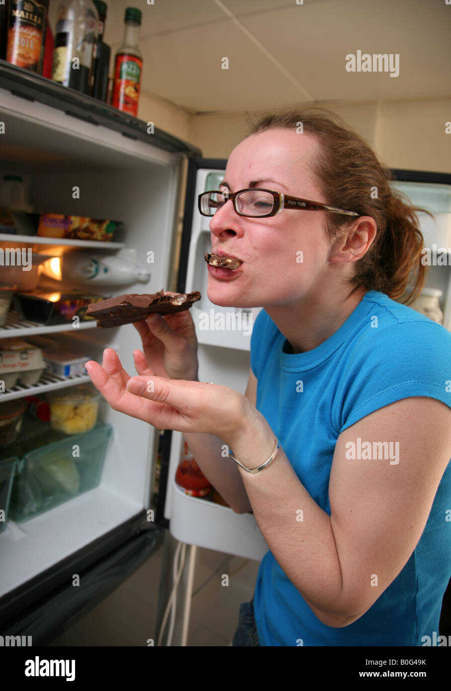 Bulimic teenager stuffing her face with a large bar of chocolate from the fridge Stock Photo