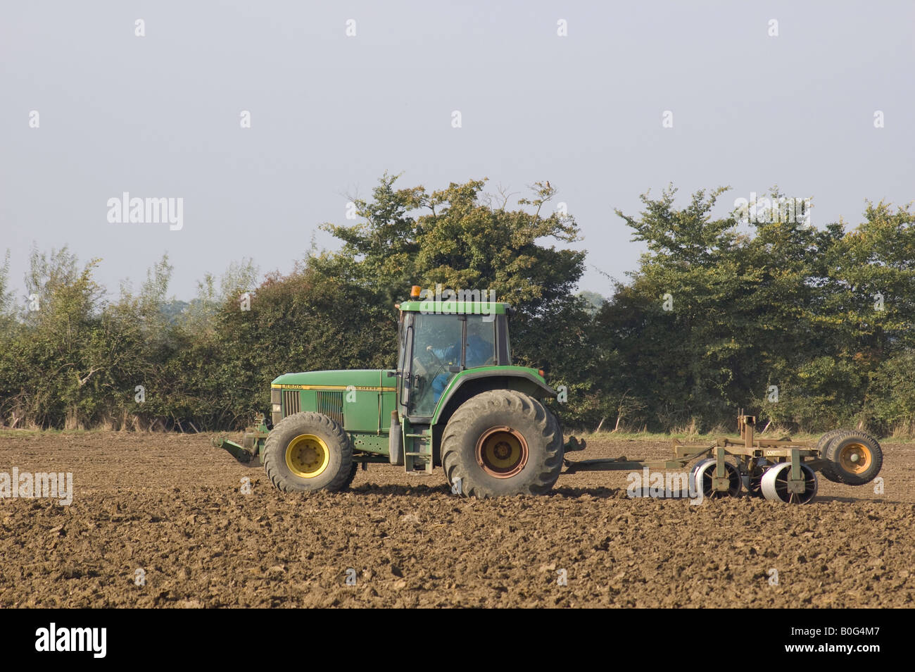John Deere tractor rolling a ploughed field, Suffolk Stock Photo