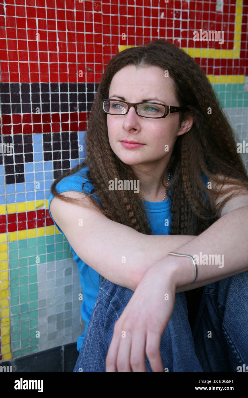 Caucasian female teenager looking upset sitting on the floor of a graffiti covered underpass on a council estate Stock Photo