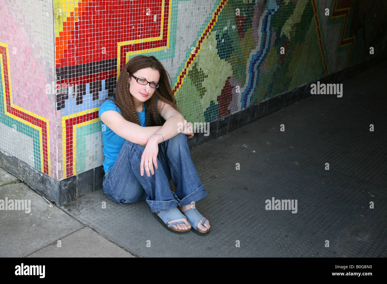 Caucasian female teenage looking upset sitting on the floor of a graffiti covered underpass on a council estate Stock Photo
