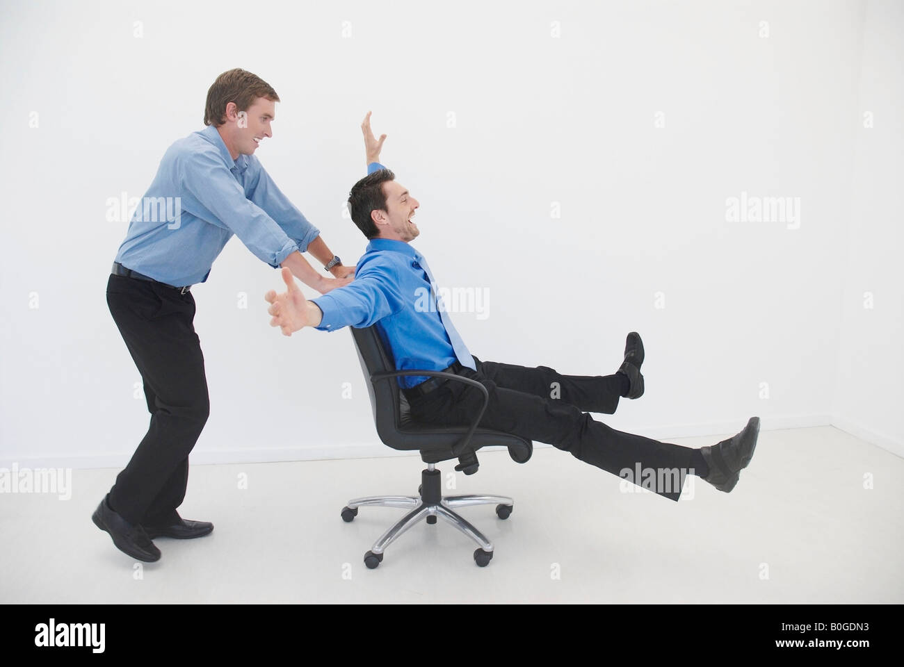Man pushes man in office chair Stock Photo