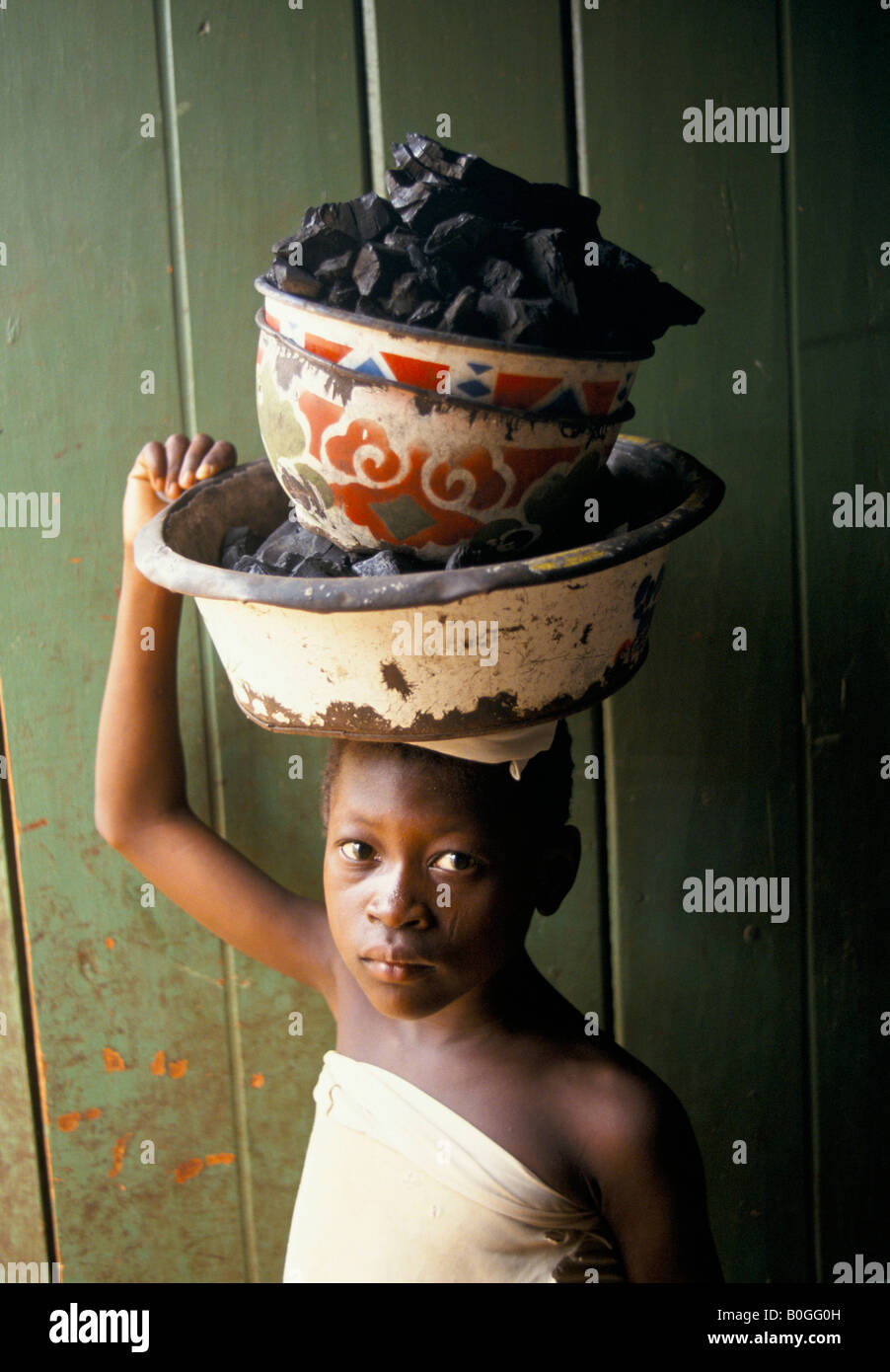 A portrait of a child carrying bowls of charcoal on her head, Ghana. Stock Photo