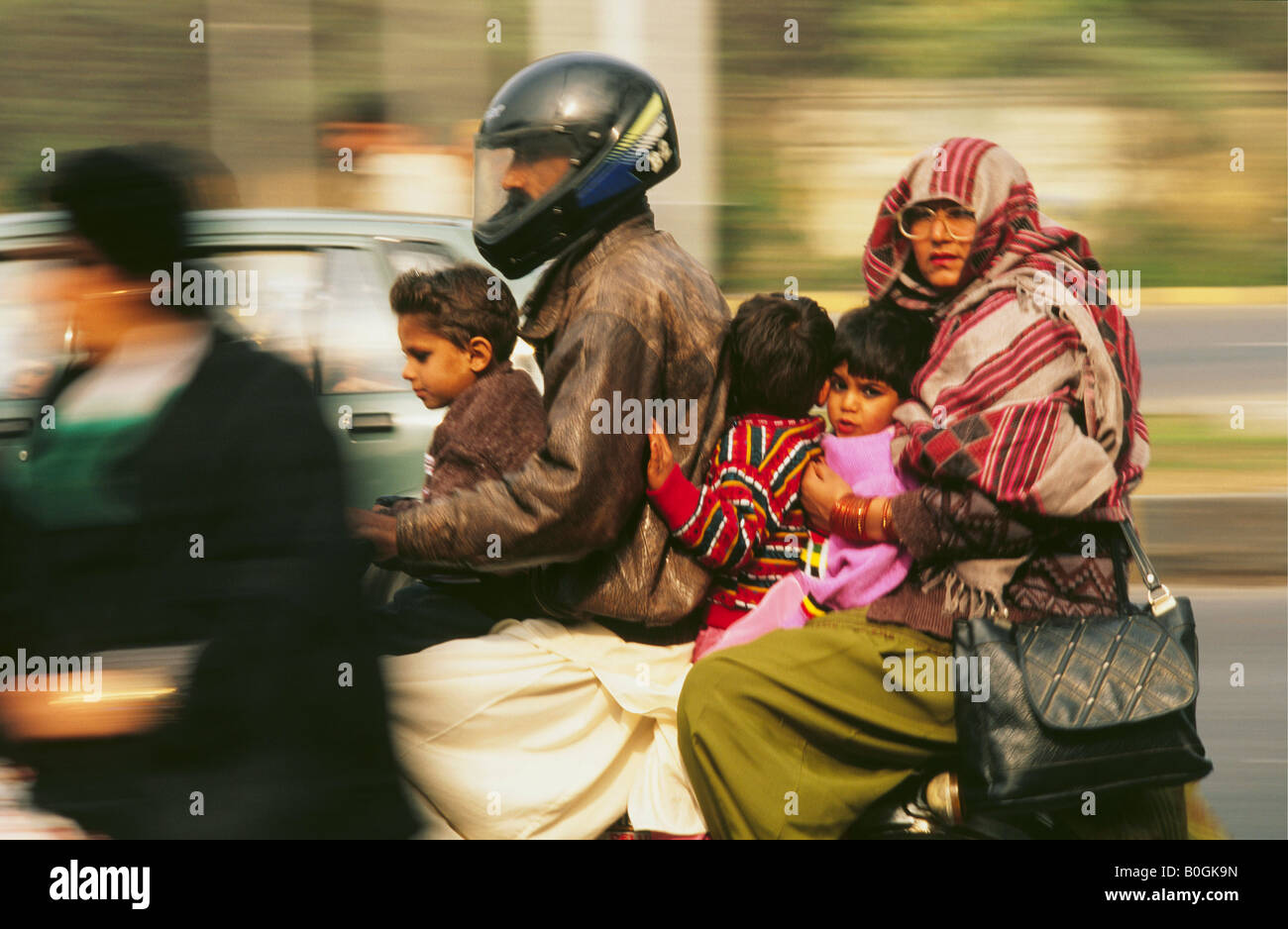 A man wearing a crash helmet, transporting his family on a scooter, Pakistan. Stock Photo