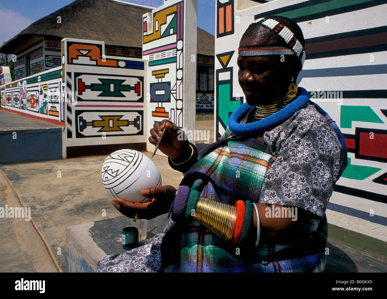 A Ndebele woman painting an egg outside a house, South Africa. Stock Photo