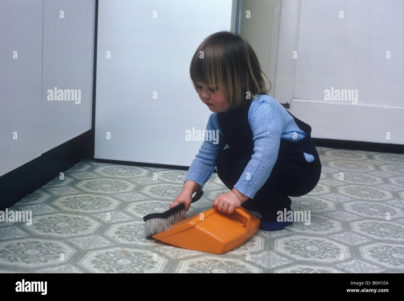 little girl sweeping kitchen floor with dustpan and brush Stock Photo