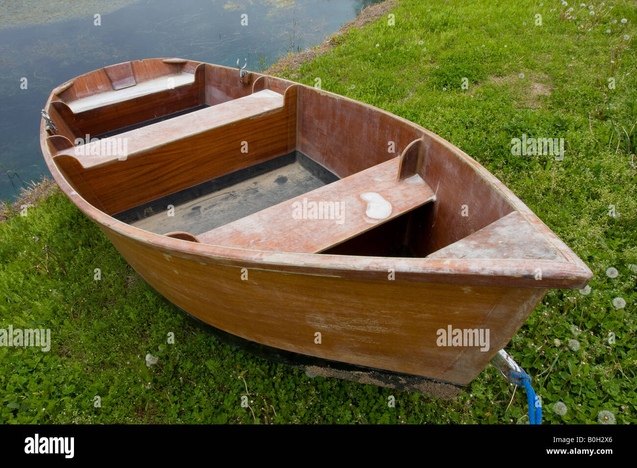 An old row boat sits next to a pond With this wide angle view you can see that the boat is in need of repair Stock Photo