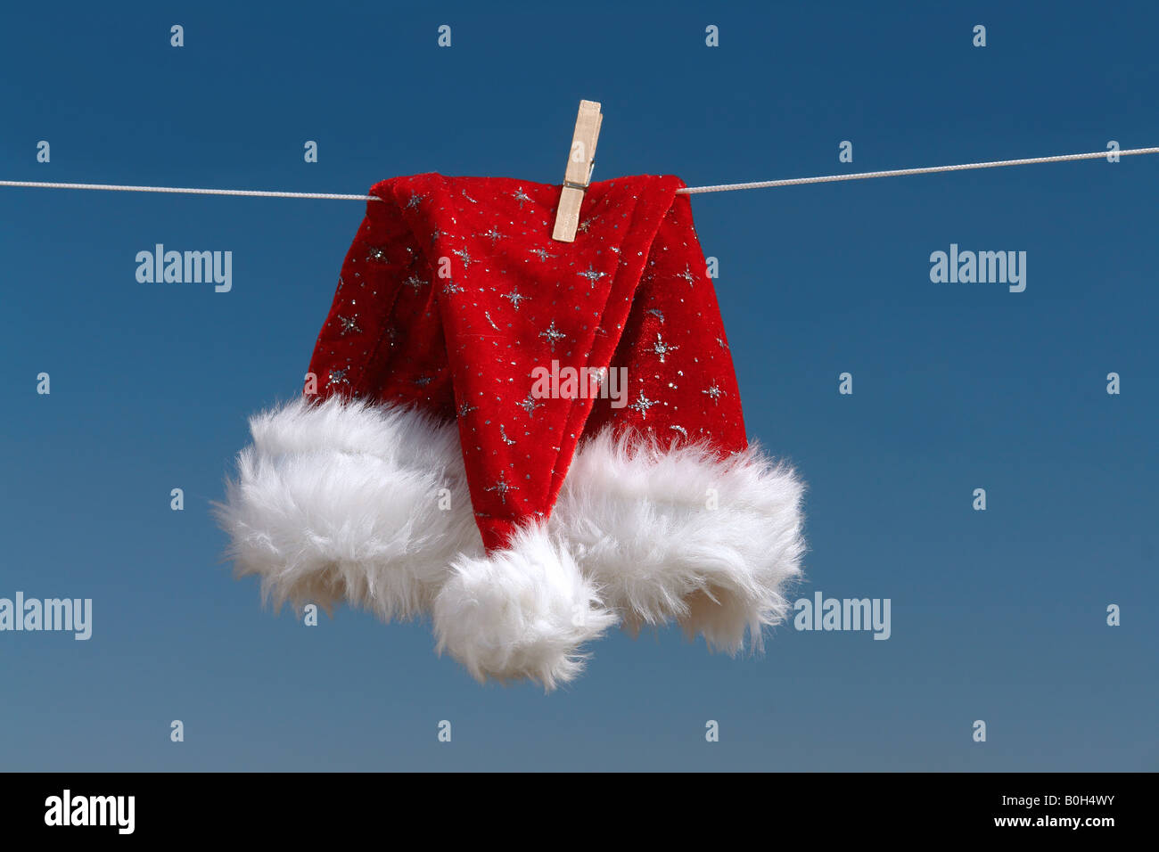 Red santa claus hat drying in the open air hanging on clothes line affixed with wooden peg Stock Photo