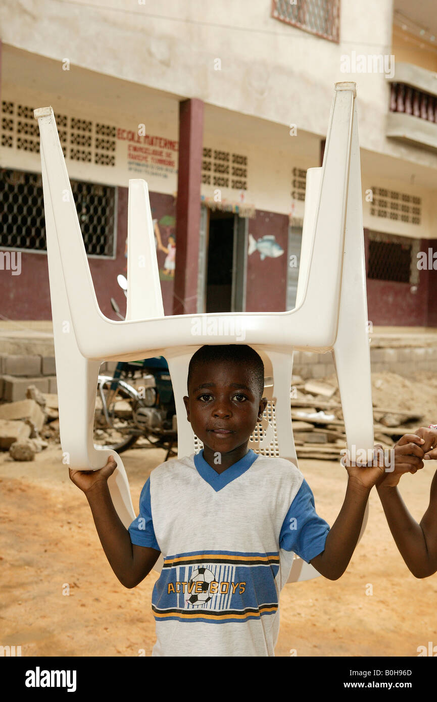 Young boy carrying a plastic chair on his head, Douala, Cameroon, Africa Stock Photo