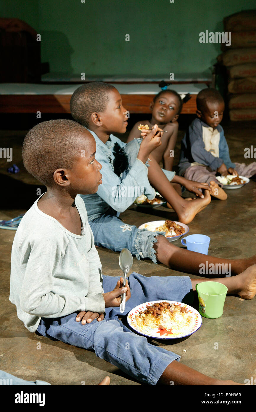 Children sitting on the floor eating their meal at an AIDS / HIV orphanage in Douala, Cameroon, Africa Stock Photo