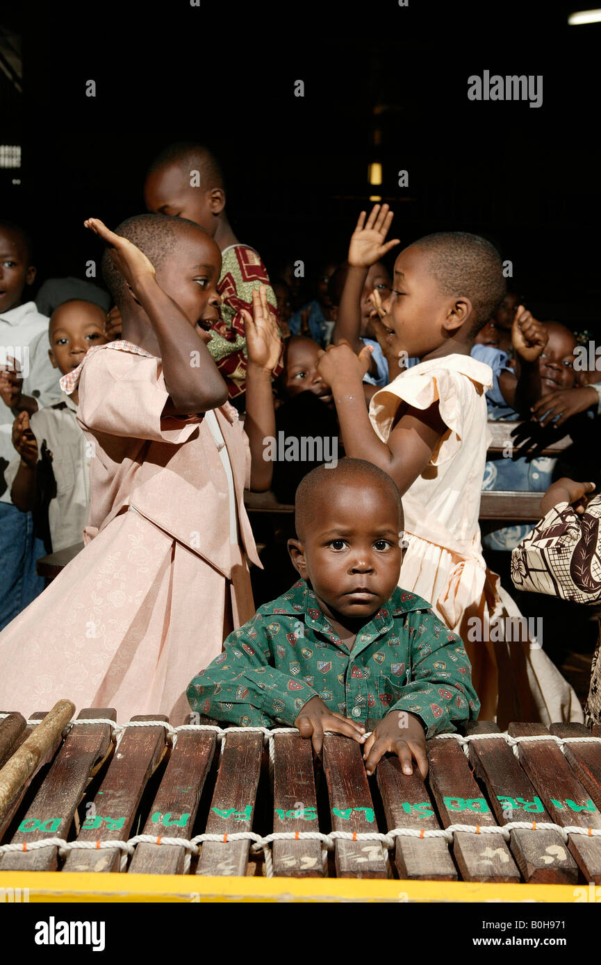 Young boy leaning on a marimba in front of two young girls dancing during a church service in Douala, Cameroon, Africa Stock Photo