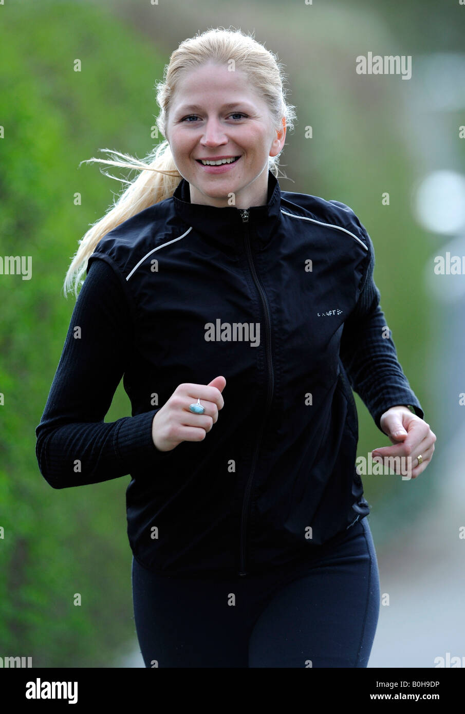 Young, smiling blonde woman wearing black tracksuit jogging Stock Photo
