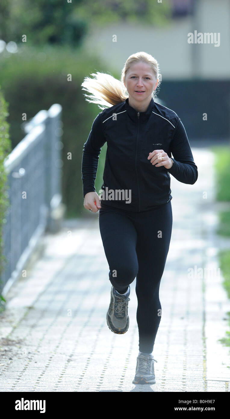 Young, blonde woman wearing black tracksuit jogging Stock Photo